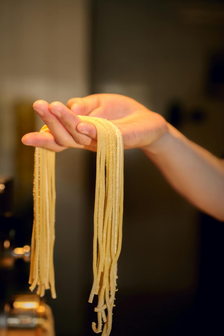 Close-up of hand holding freshly made pasta noodles indoors.